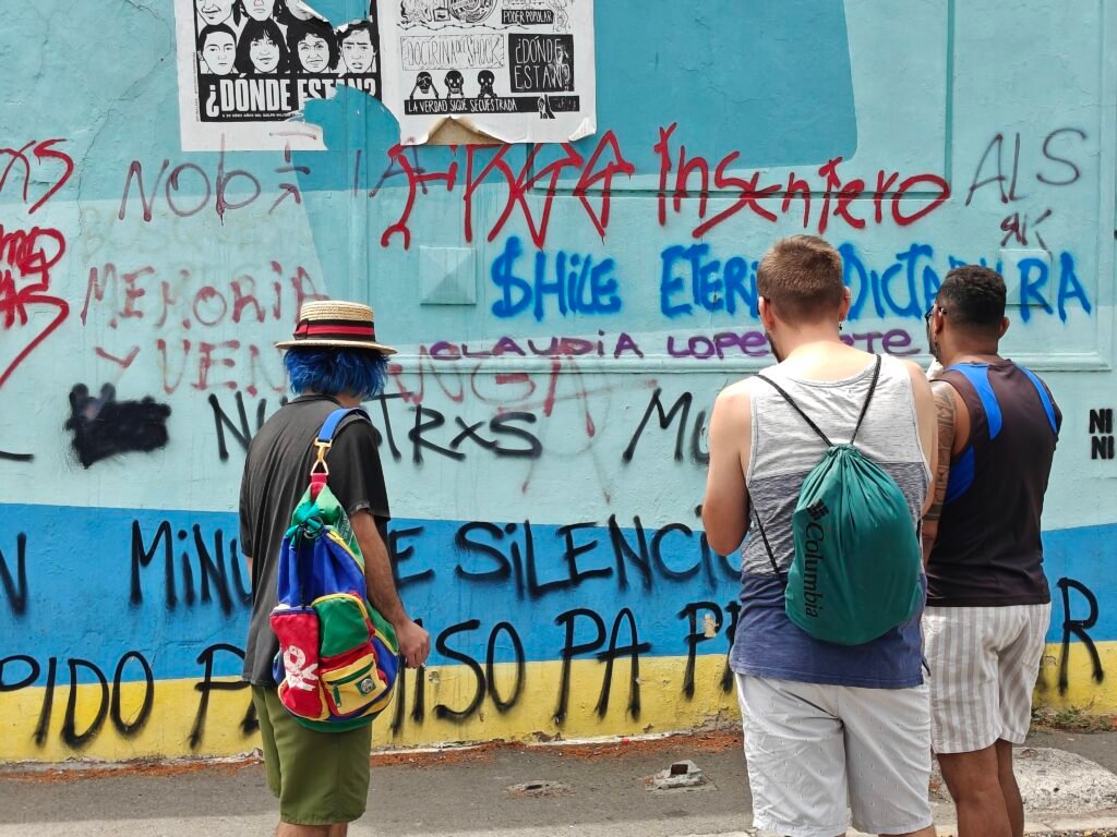 Tres personas observando un mural de graffitis en una calle de Santiago