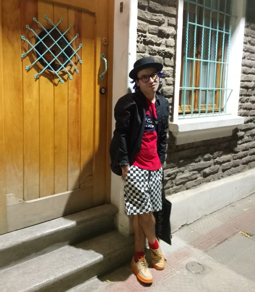 Hombre joven apoyado en una puerta antigua de madera, en una calle empedrada de Santiago